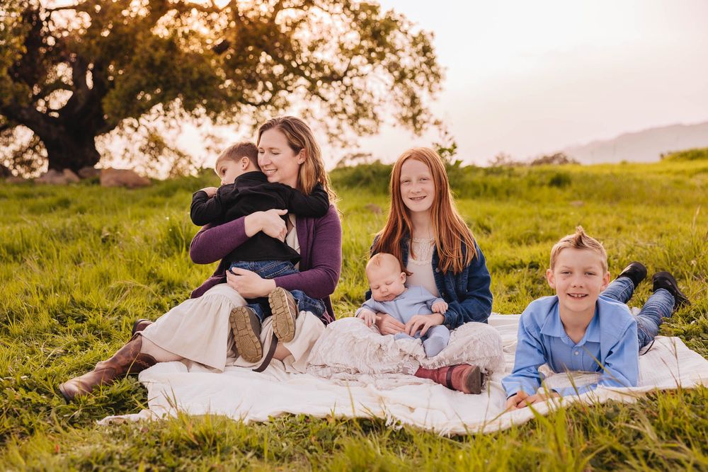 Family relaxes on a picnic blanket in a grassy field at sunset.