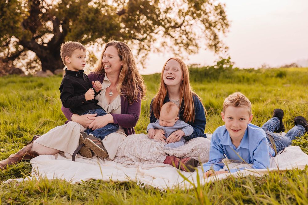 Family relaxing together on blankets in a sunny meadow.
