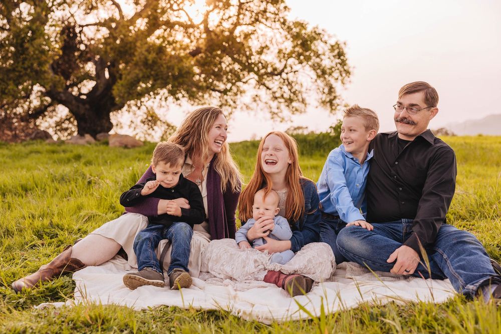Happy family enjoying time together outdoors on blanket during golden hour.