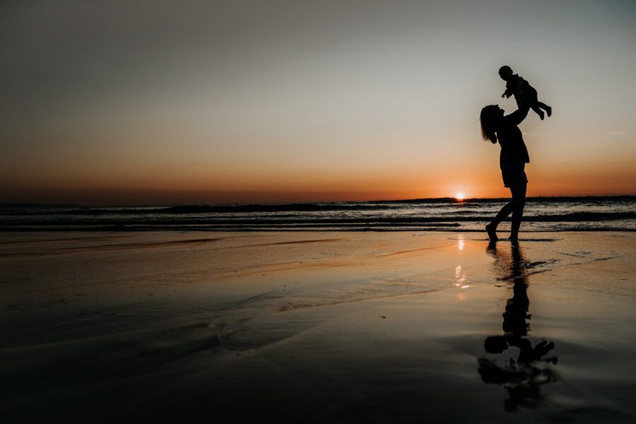 Silhouettes playing on a beach at sunset with reflections in the wet sand.