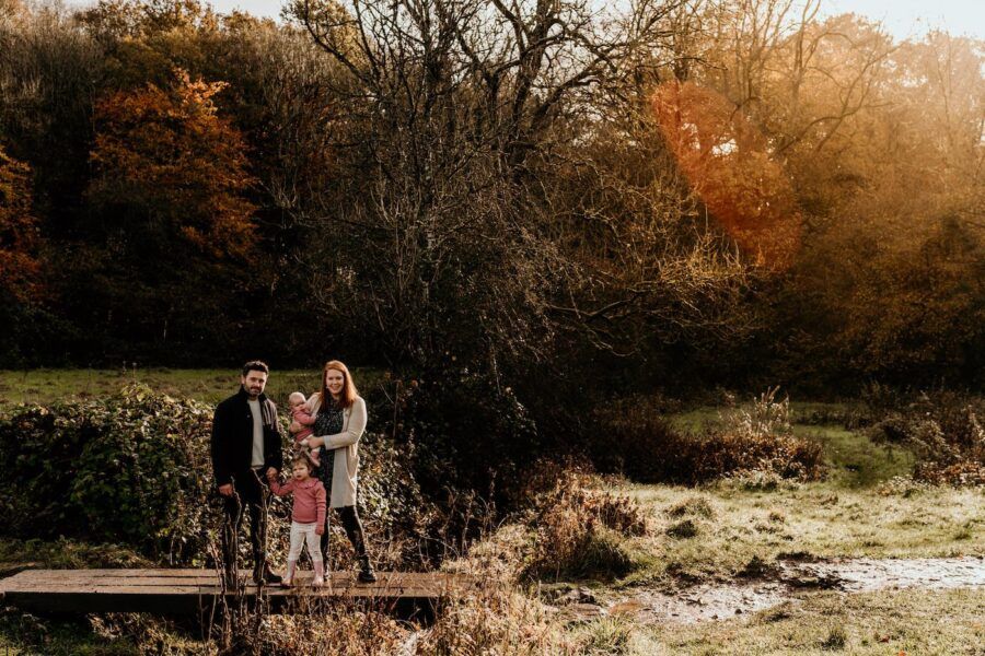 Family enjoying a sunset photo session in an autumn forest setting with golden light filtering through trees.