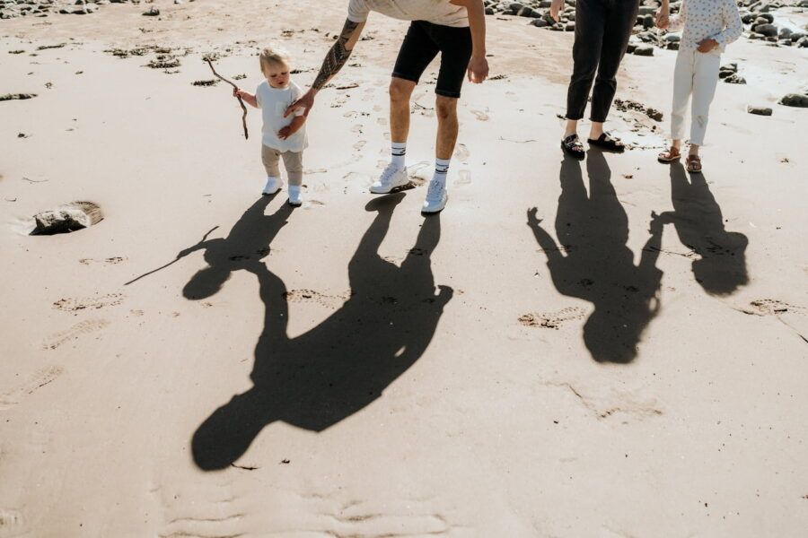 Family casting long shadows while walking together on a sandy beach during a photo session.
