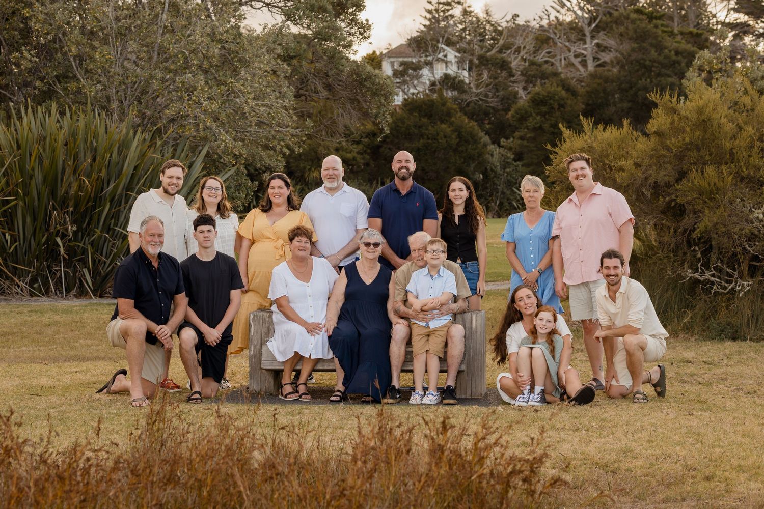 Extended family photoshoot of a family of 17 during golden hour taken outside with greenery surrounding the family. All smiles