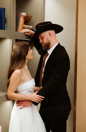 Intimate couple moment captured in front of floor-to-ceiling bookshelves, showing contrasting black and white attire.