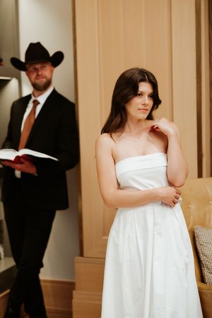 Woman in strapless white dress poses thoughtfully in a room with built-in bookshelves.