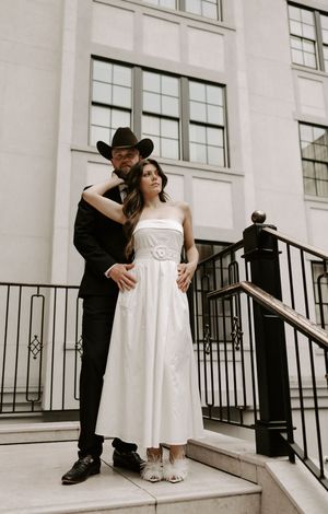 Couple embracing on stone steps with iron railing outside building entrance.
