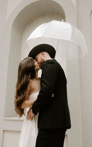 A romantic couple embraces under white arches in formal wedding attire.