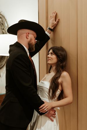 A couple in formal wear shares an intimate moment against a wooden wall.