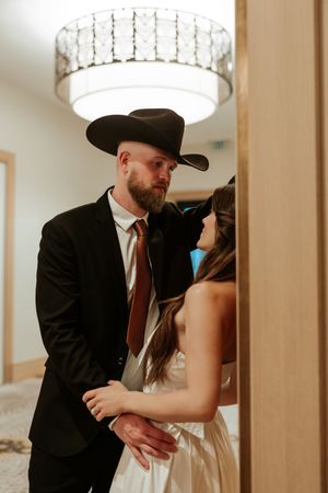 A romantic couple poses under crystal chandelier lighting in formal attire.