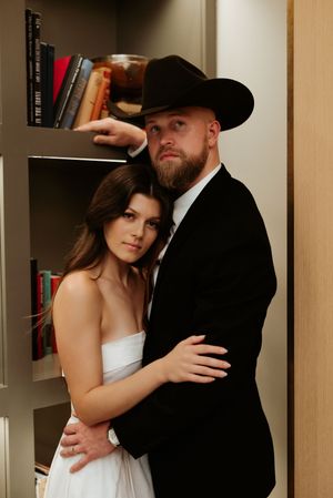 A couple poses together in a library setting with wooden bookshelves.