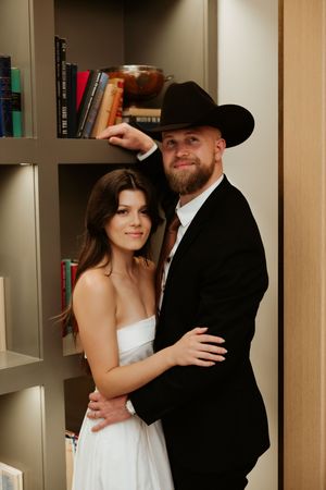 Wedding couple embraces while standing in front of floor-to-ceiling bookshelves.