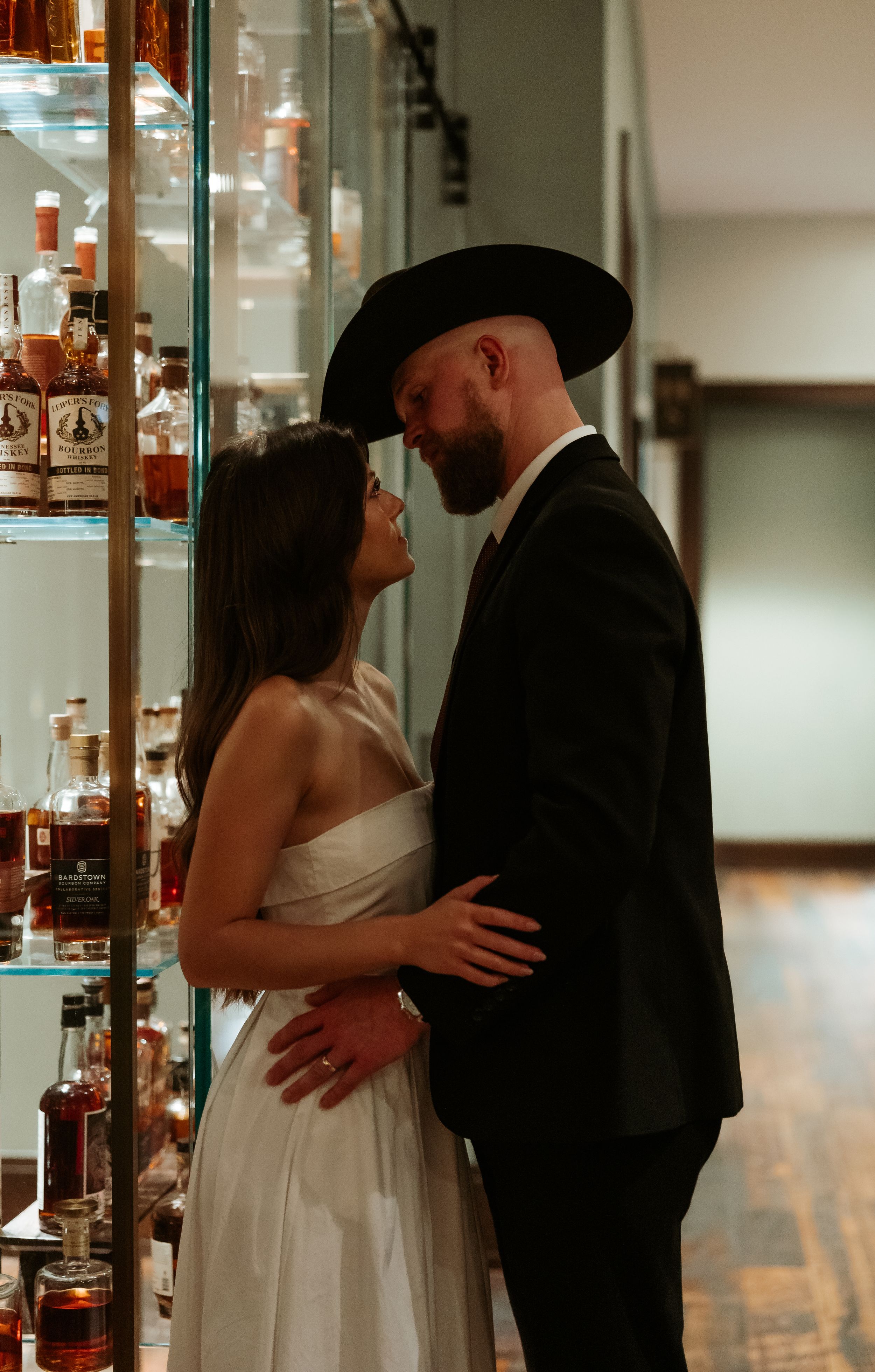 A tender moment between newlyweds beside a glass display, with western-style formal attire.