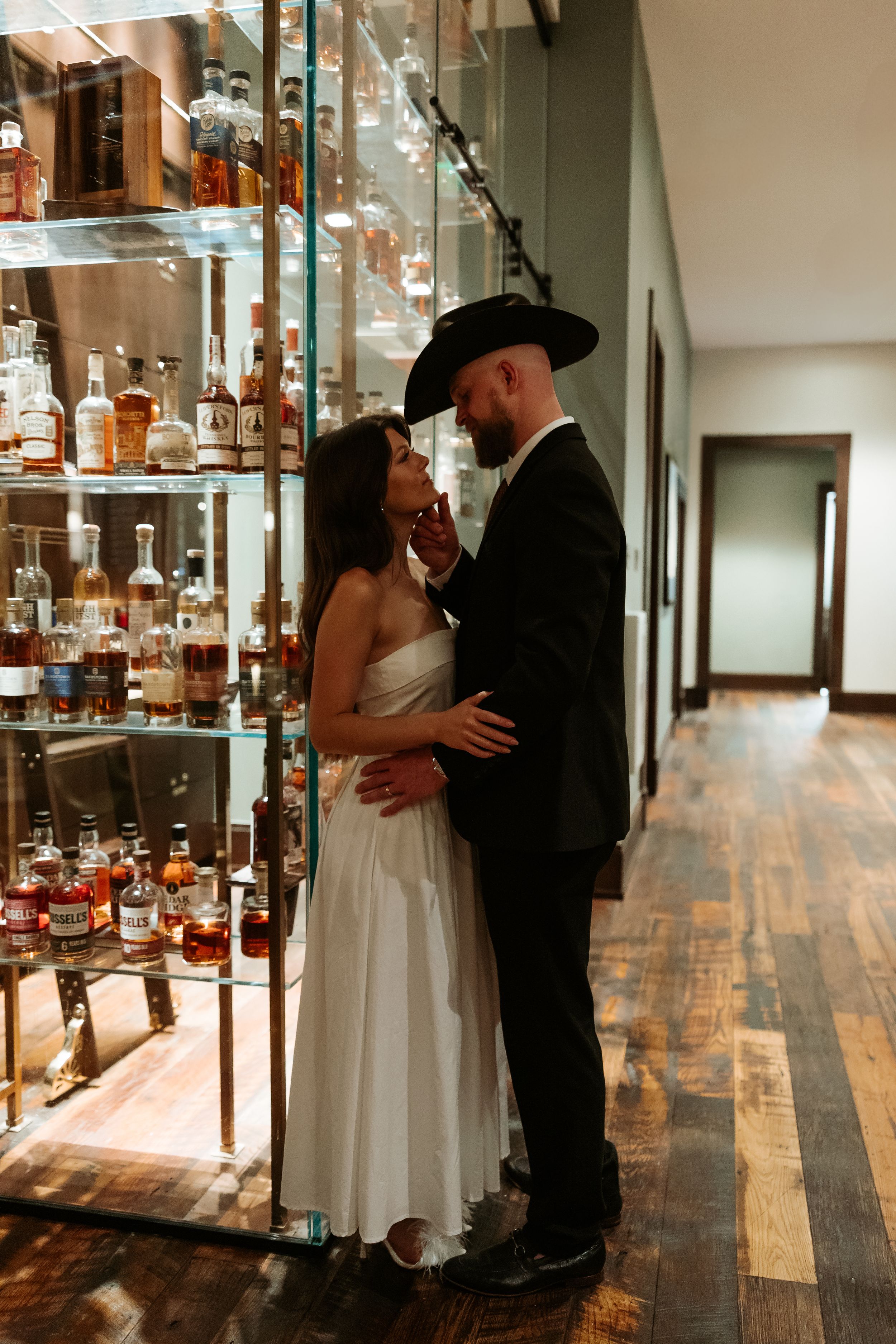 A couple shares an intimate moment beside a display case of spirits and bottles.