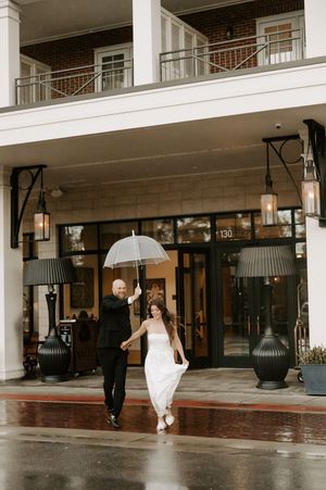 A couple dances with umbrellas on a rainy day outside a brick and white columned building.