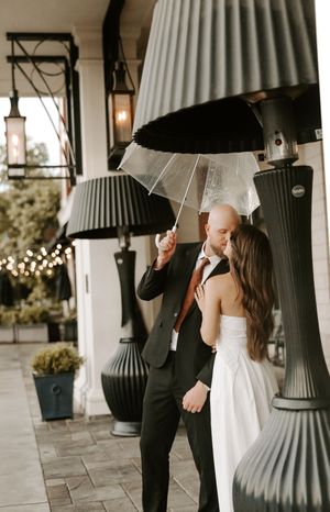 A couple poses playfully with umbrellas between modern architectural columns.