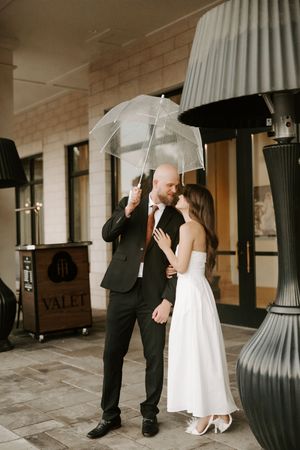 Two people dance and laugh while holding umbrellas under a covered walkway.