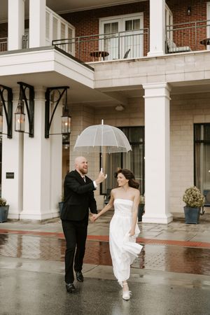 Couple dances beneath white columns during their rainy day wedding celebration.