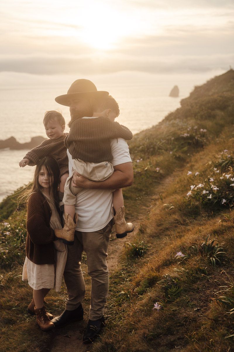A family enjoys sunset views on a scenic coastal trail overlooking misty ocean cliffs and wildflowers.