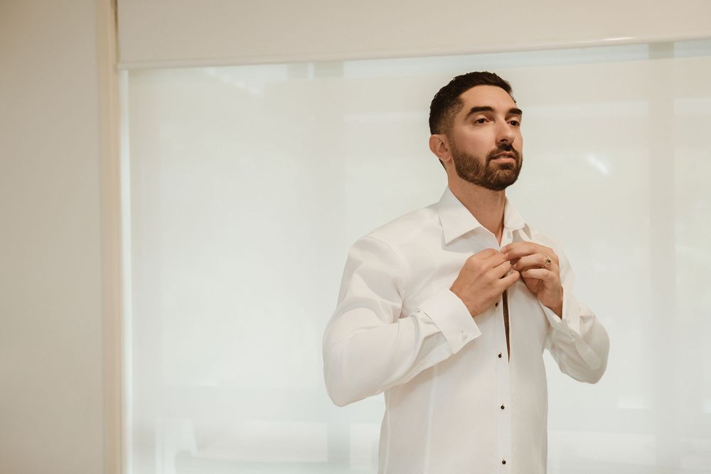 Getting dressed for a formal event in a crisp white dress shirt against light background.