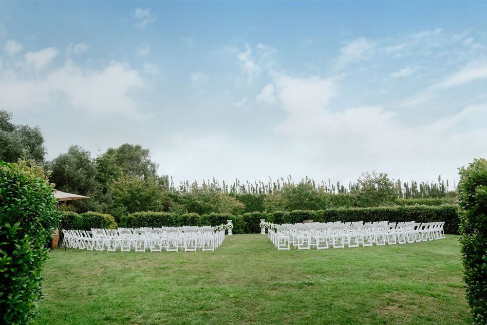 White folding chairs arranged in rows on a grassy lawn for an outdoor wedding ceremony under blue skies.