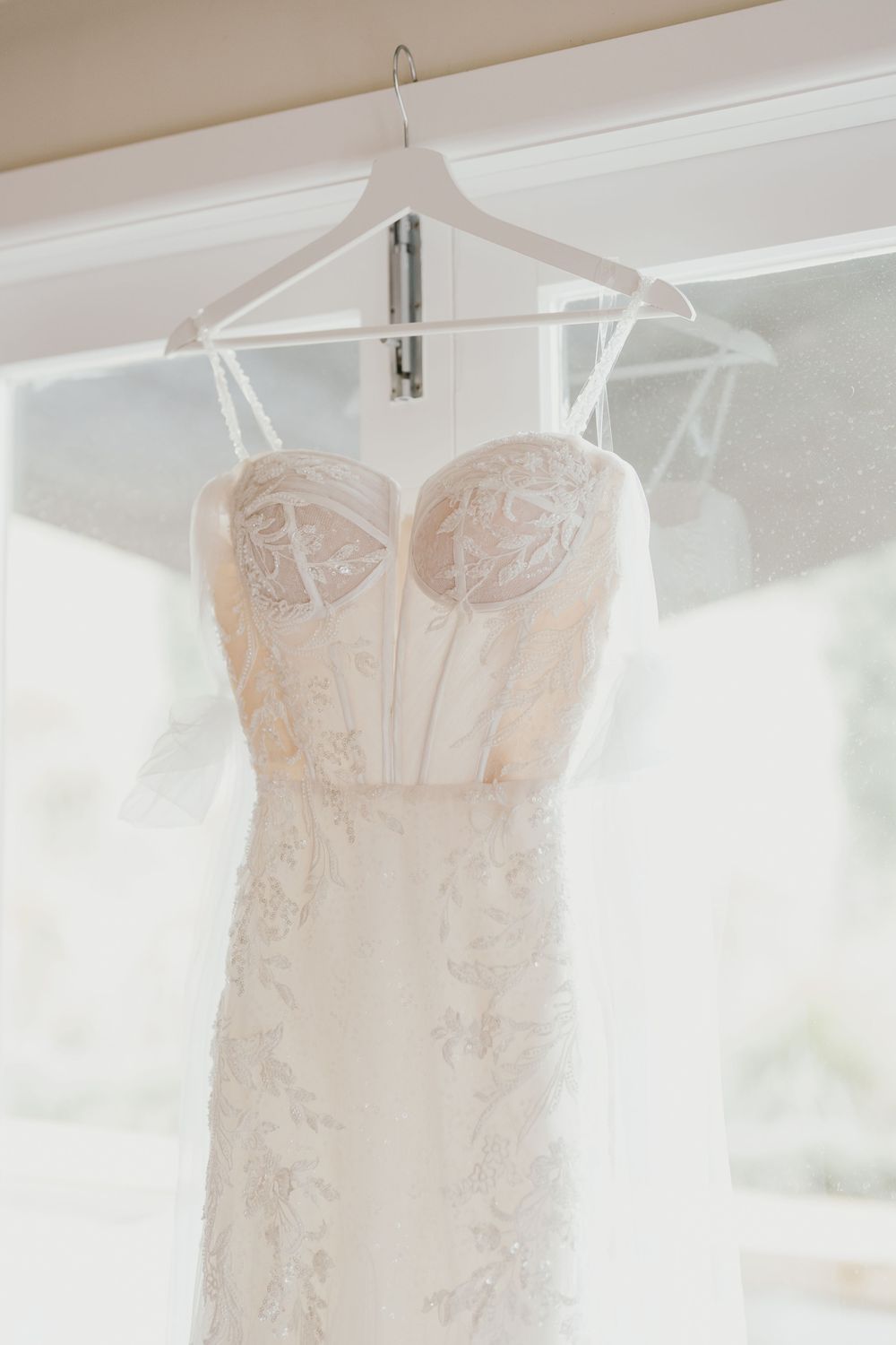 Close-up details of an elegant strapless wedding gown with delicate floral embroidery hanging on display.