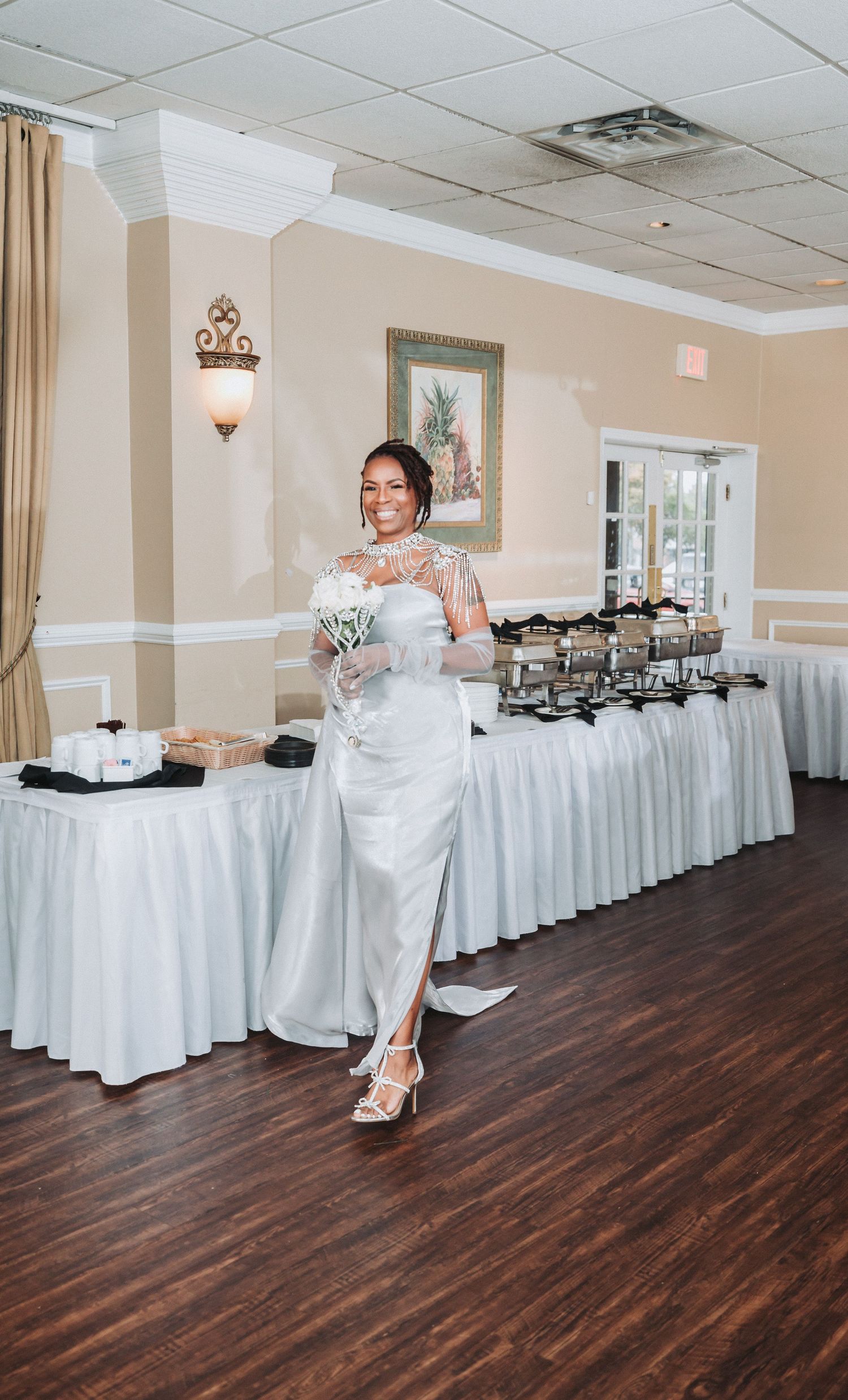 A wedding reception venue with white table linens and buffet tables set up against beige walls with elegant lighting.