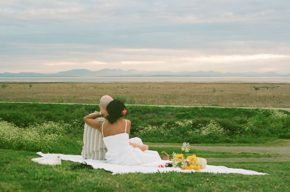 A serene picnic setting with a couple overlooking mountains and fields at sunset.
