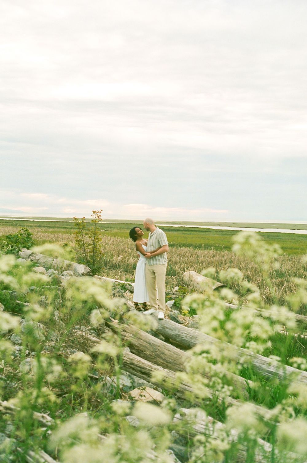 A romantic embrace among wildflowers with mountains in the background.