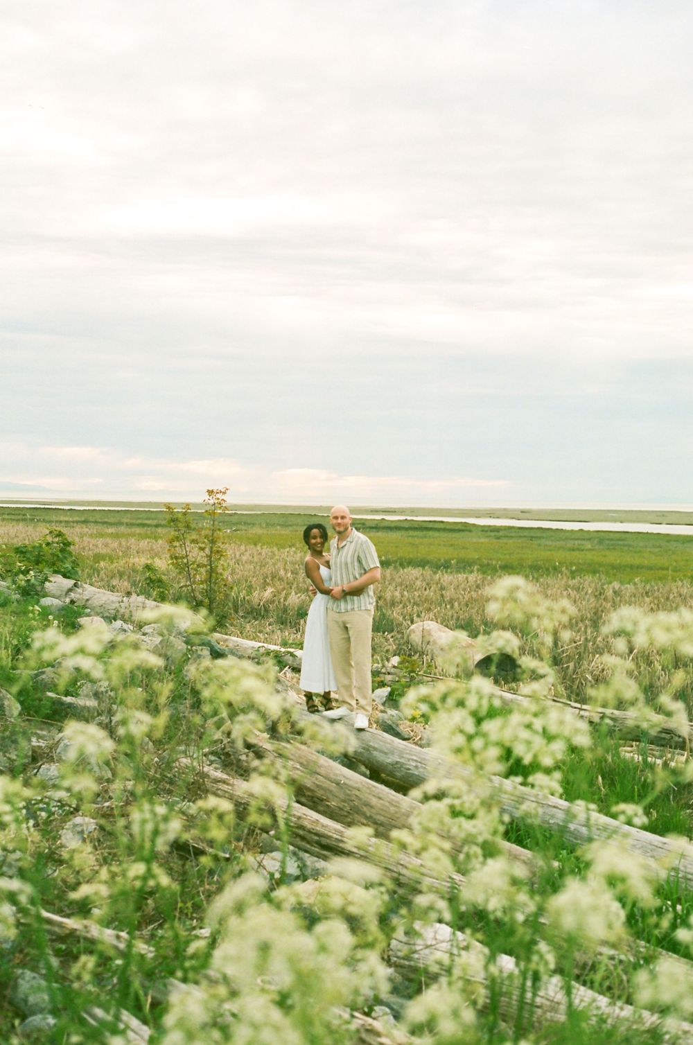 Two people walking through a meadow of white flowers with a serene landscape in the background.