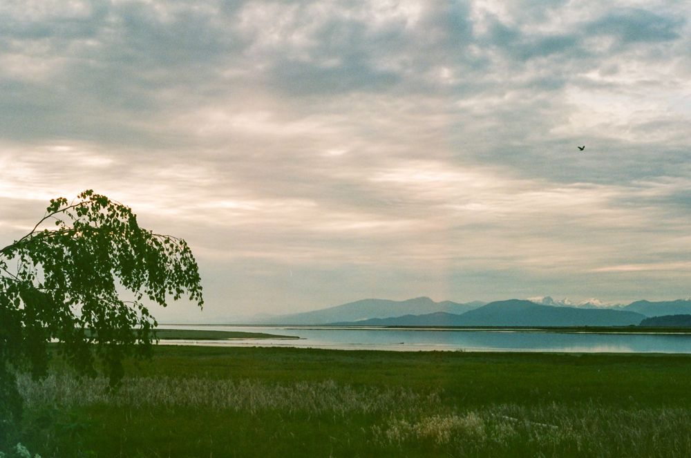 Dramatic panoramic landscape view of mountains and a lake under cloudy skies.