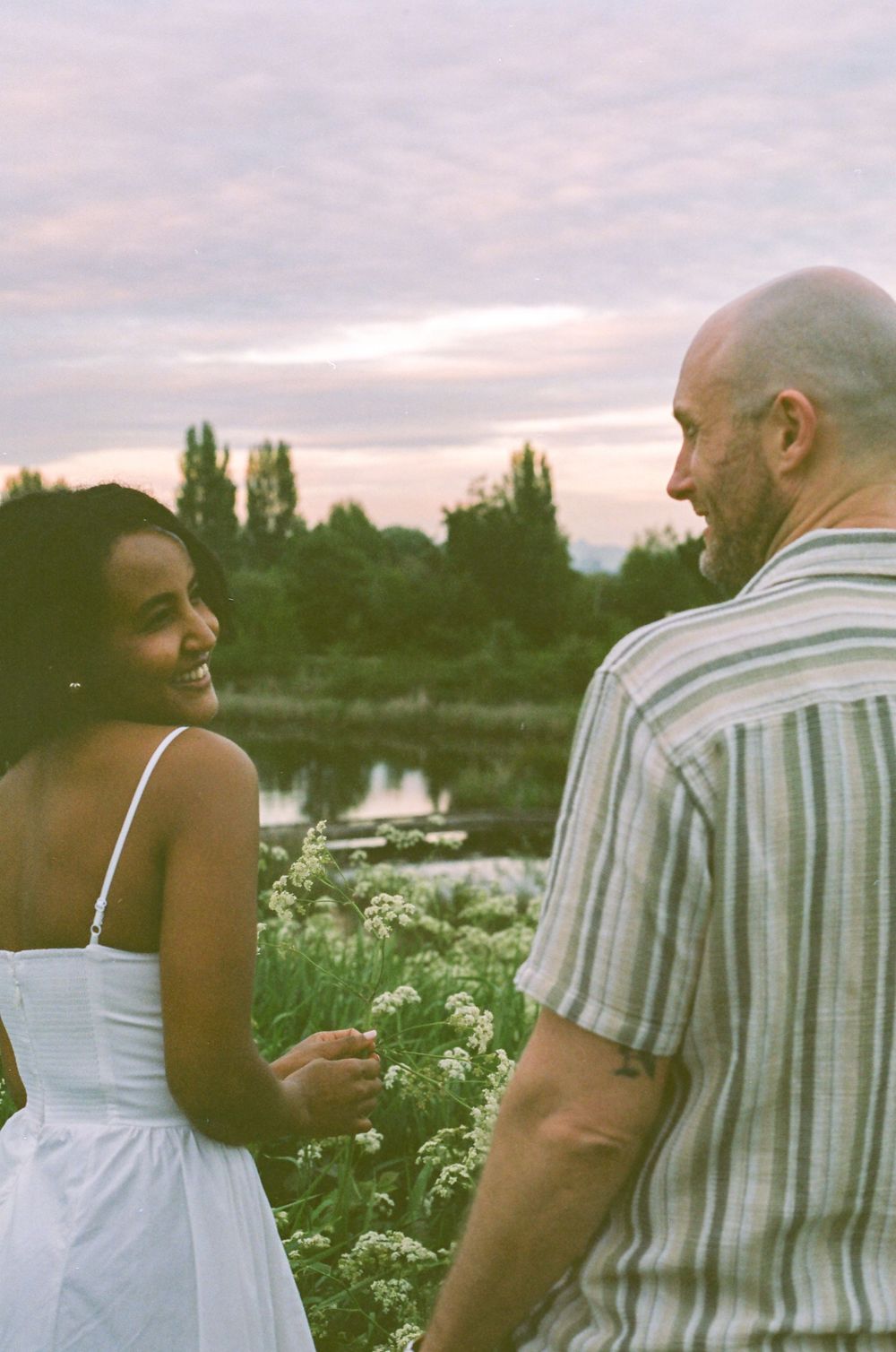 Two people share an intimate moment in a field of flowers during sunset.
