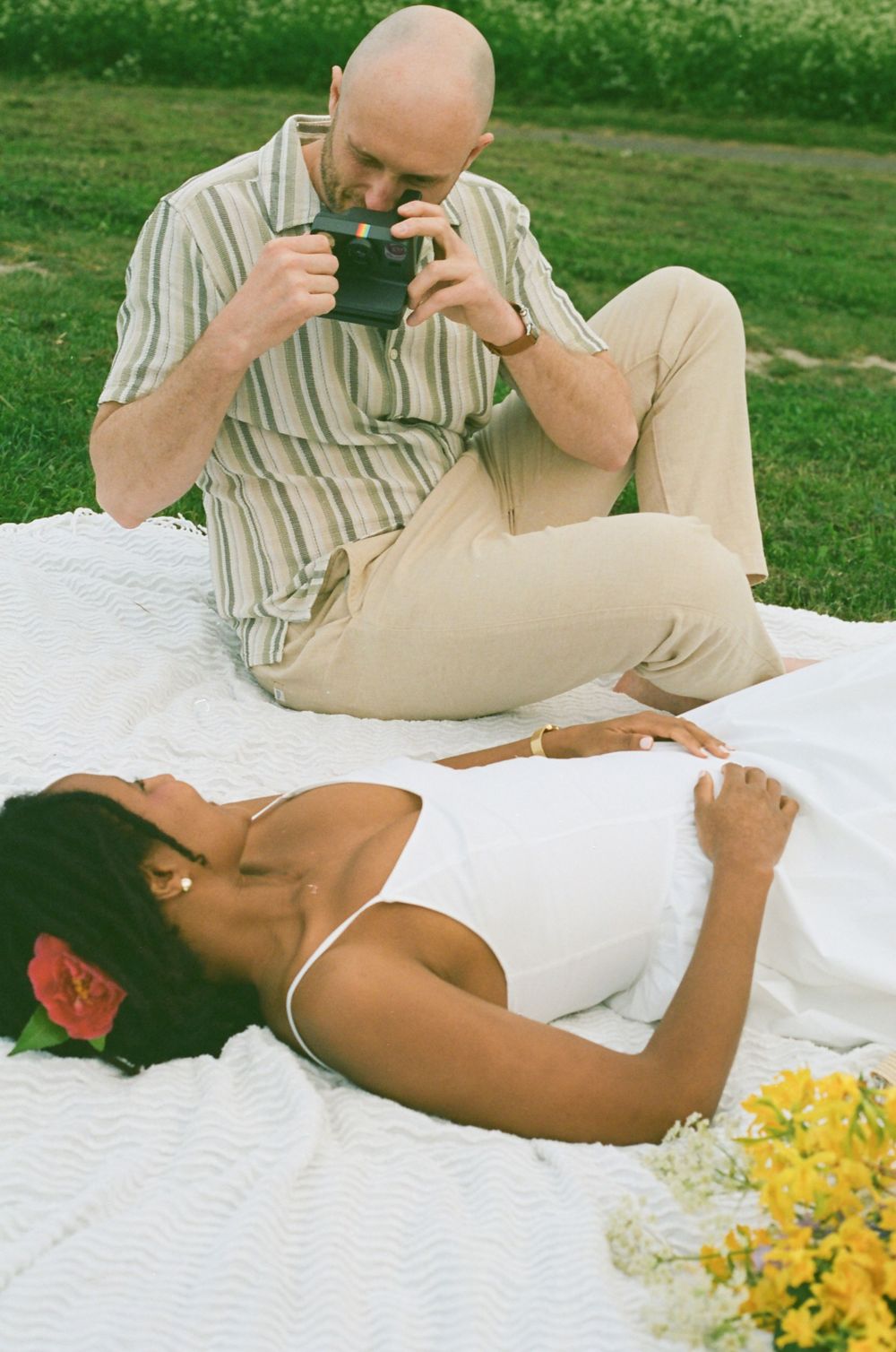 A candid moment of a couple laughing together during a picnic on a white blanket outdoors.