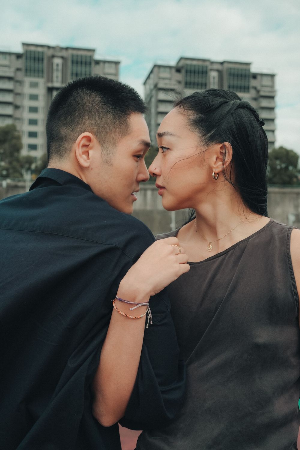 An intimate couple's portrait showing a tender moment between partners against a city backdrop with tall buildings.