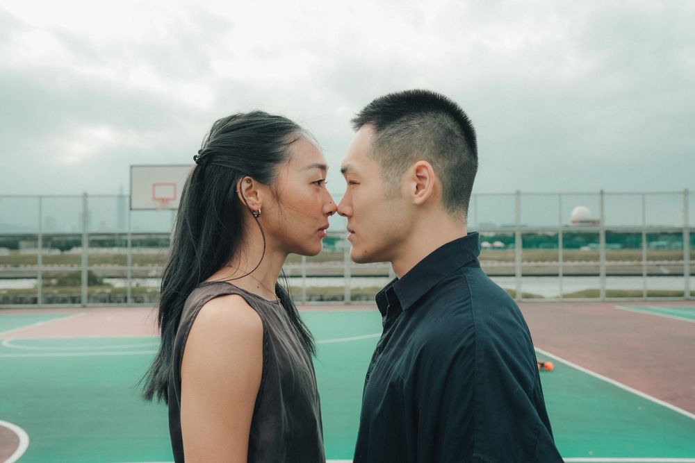 A romantic couple shares an intimate moment on an outdoor basketball court on a cloudy day.