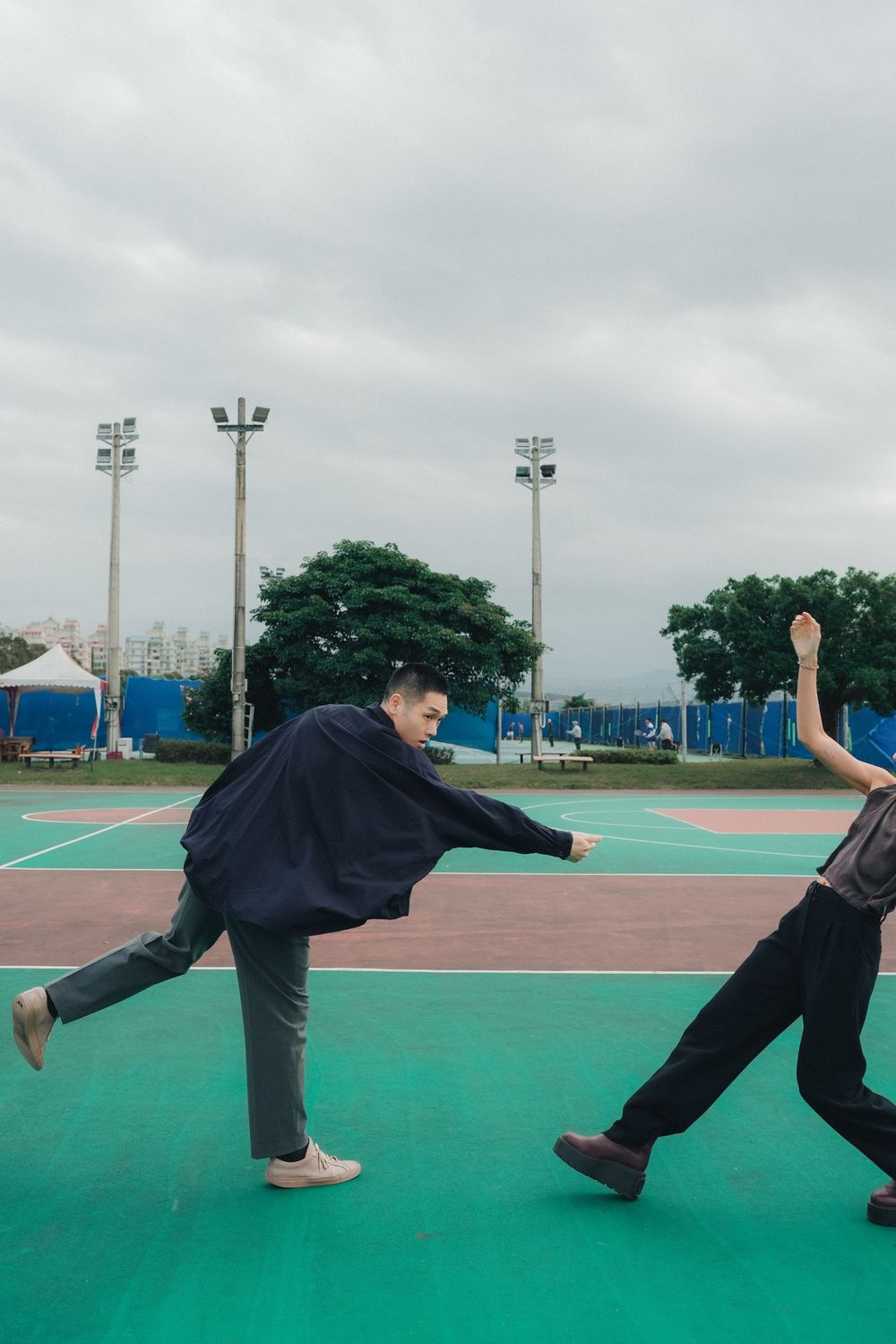 Two people practicing martial arts moves on a green outdoor court under cloudy skies with stadium lights in the background.