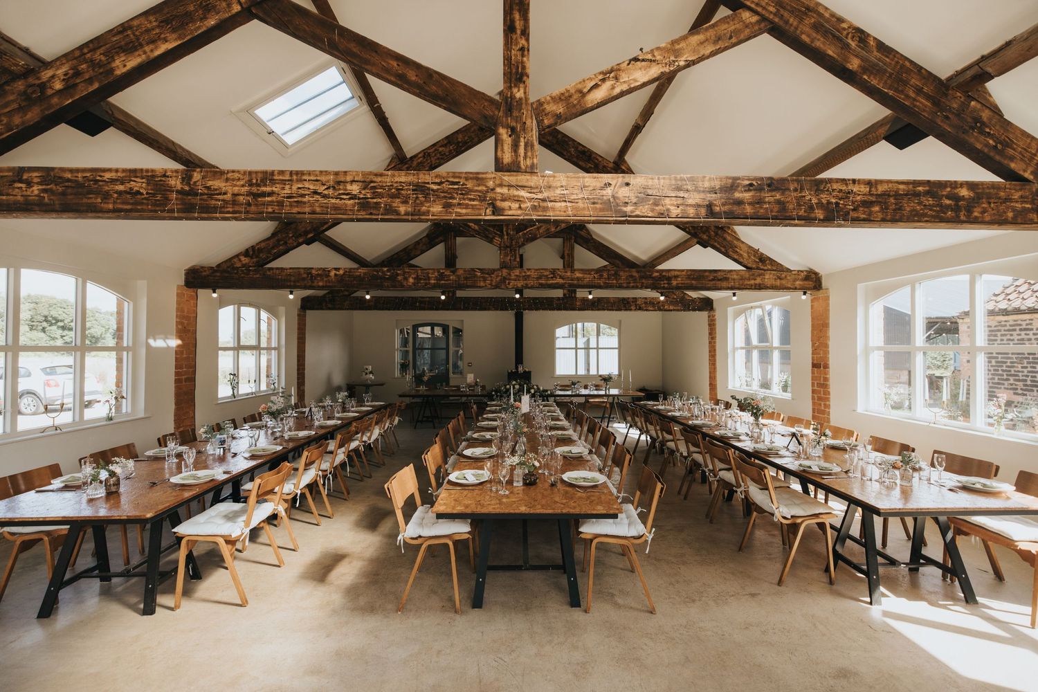 Large rustic dining space with exposed wooden beams, white walls, and natural light streaming through windows and skylights.
