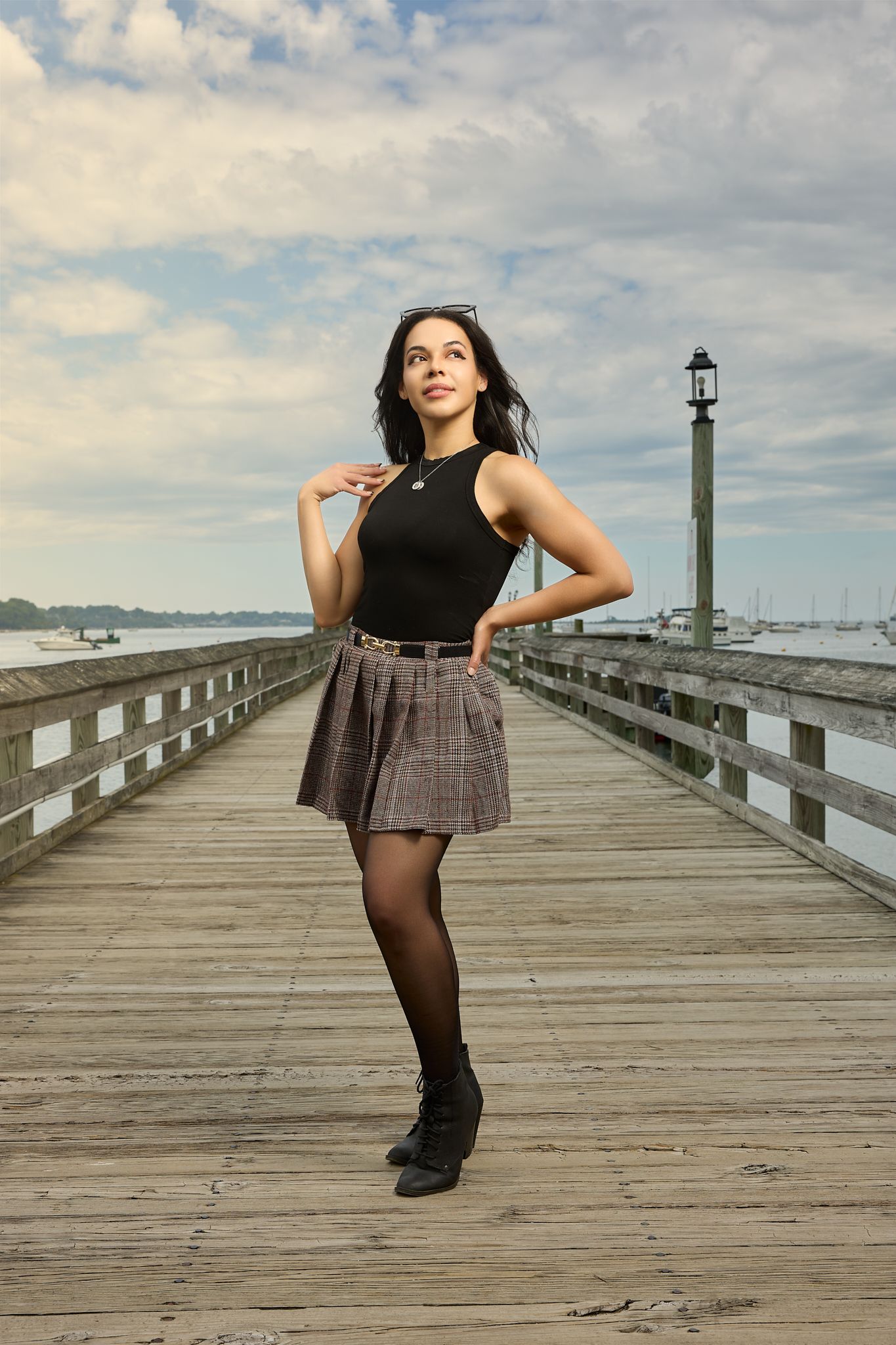 A stylish pose on a wooden pier with boats and a lighthouse in the background during golden hour.