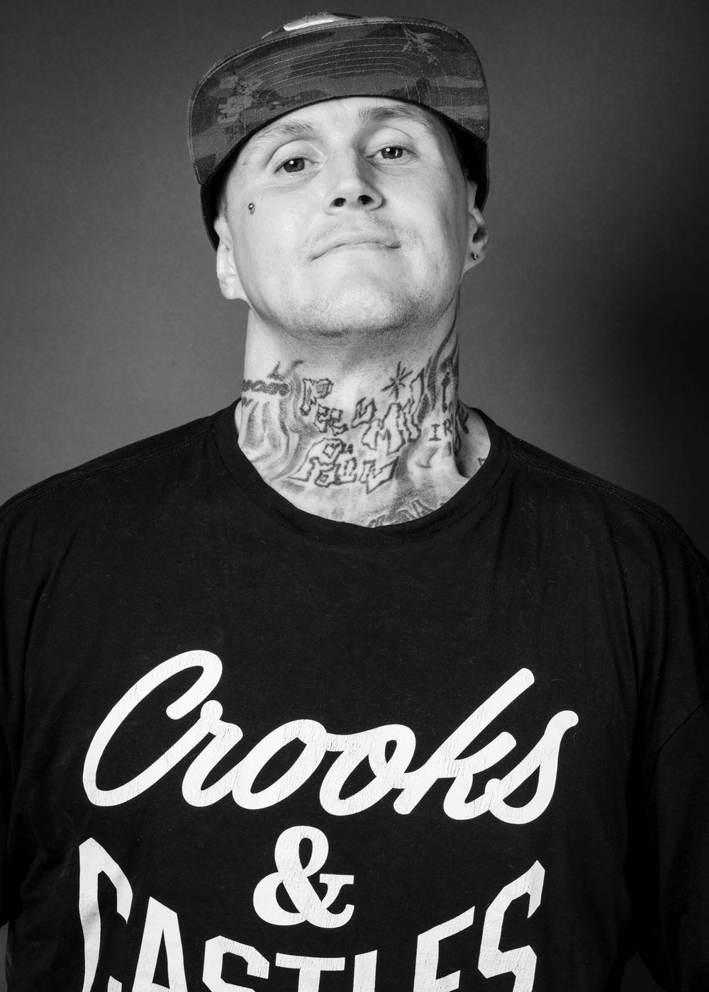 Black and white portrait of someone wearing a Crooks & Castles t-shirt and hat with visible neck tattoos. - Morgan -