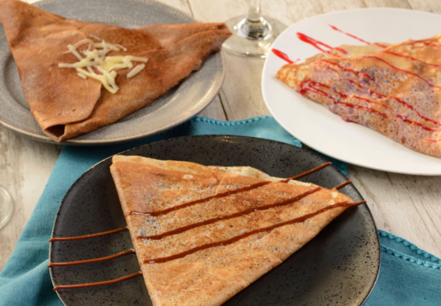 Traditional French crepes drizzled with chocolate sauce served on dark plates.