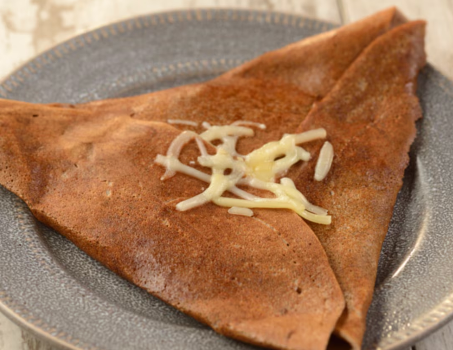 A chocolate crepe topped with shredded cheese served on a gray plate.