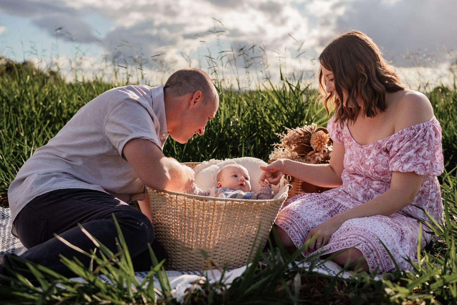 Family enjoying a relaxing summer picnic together on a grassy meadow at sunset with a picnic basket.