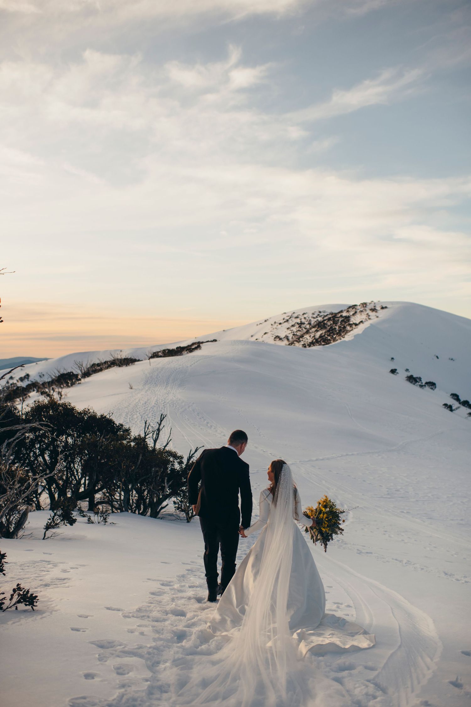 Snowy mountain landscape with wedding couple walking through pristine white slopes.