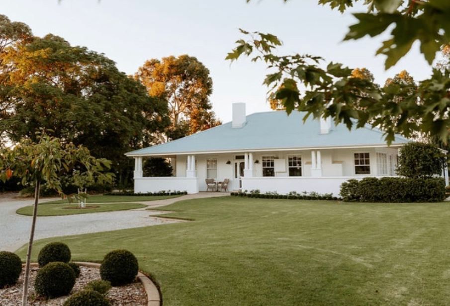 Panoramic view of white farmhouses with green lawns and autumn trees in a rural setting.
