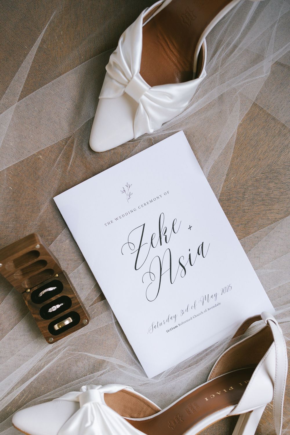 Wedding invitation and white bridal shoes arranged with veil on wooden floor.
