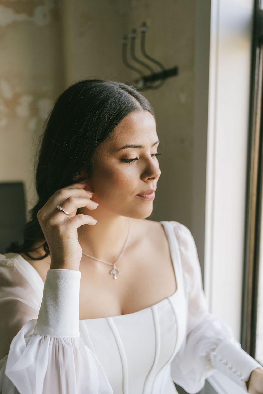 Elegant bridal portrait series in white dress by window with soft natural lighting.