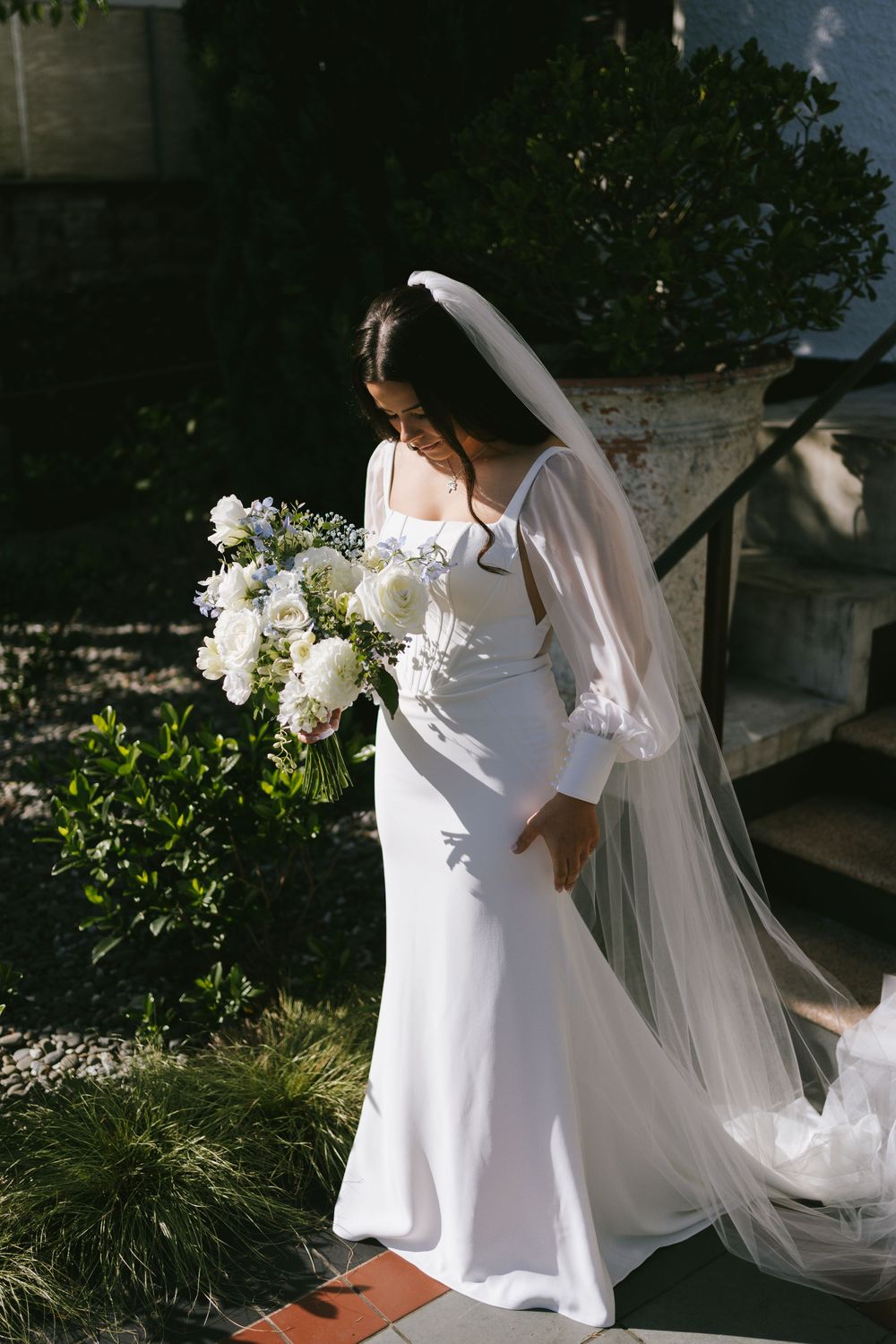 Bride in flowing white dress with long sleeves walks gracefully through garden setting.