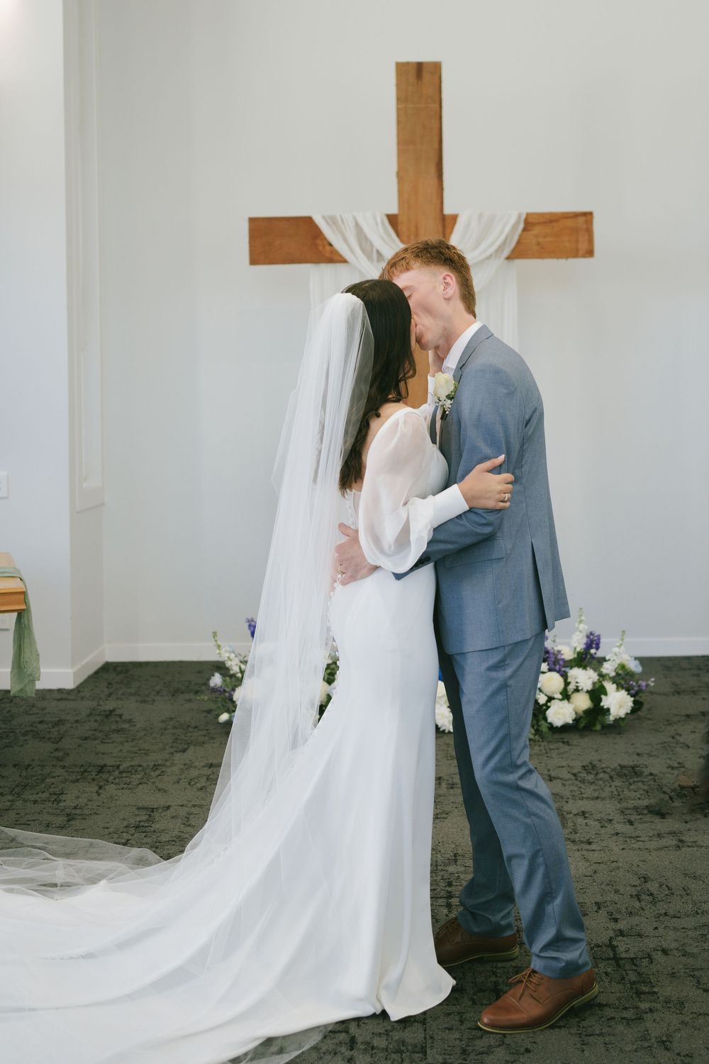 Wedding ceremony moments captured in front of wooden cross with flowing white veil.