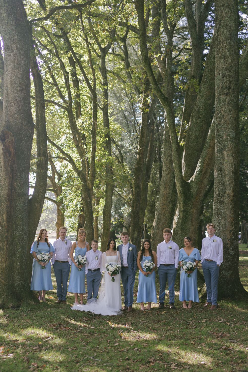 Wedding party poses in wooded setting with bridesmaids in light blue dresses.