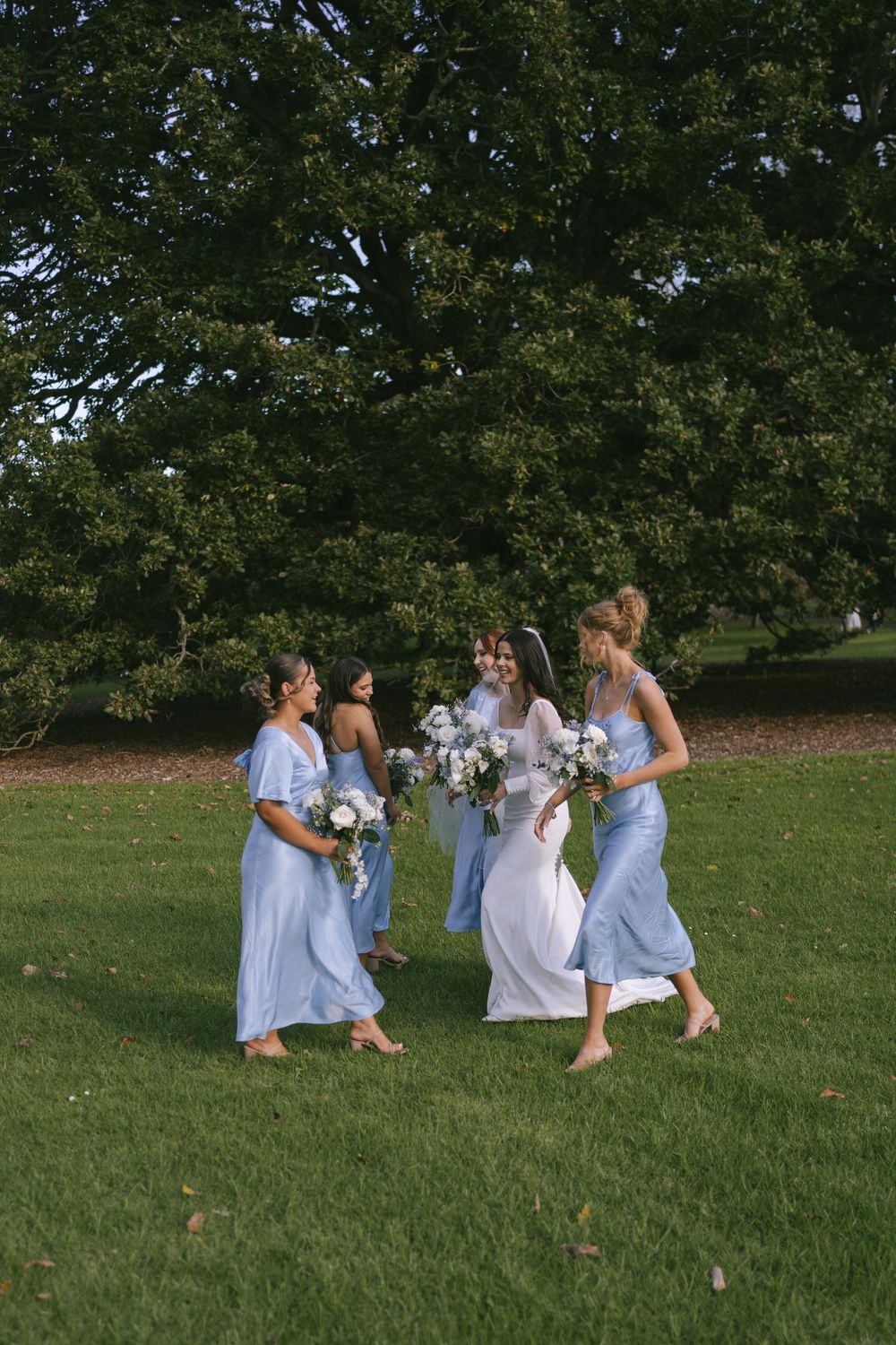 Wedding party in light blue dresses playing on a grassy hillside.