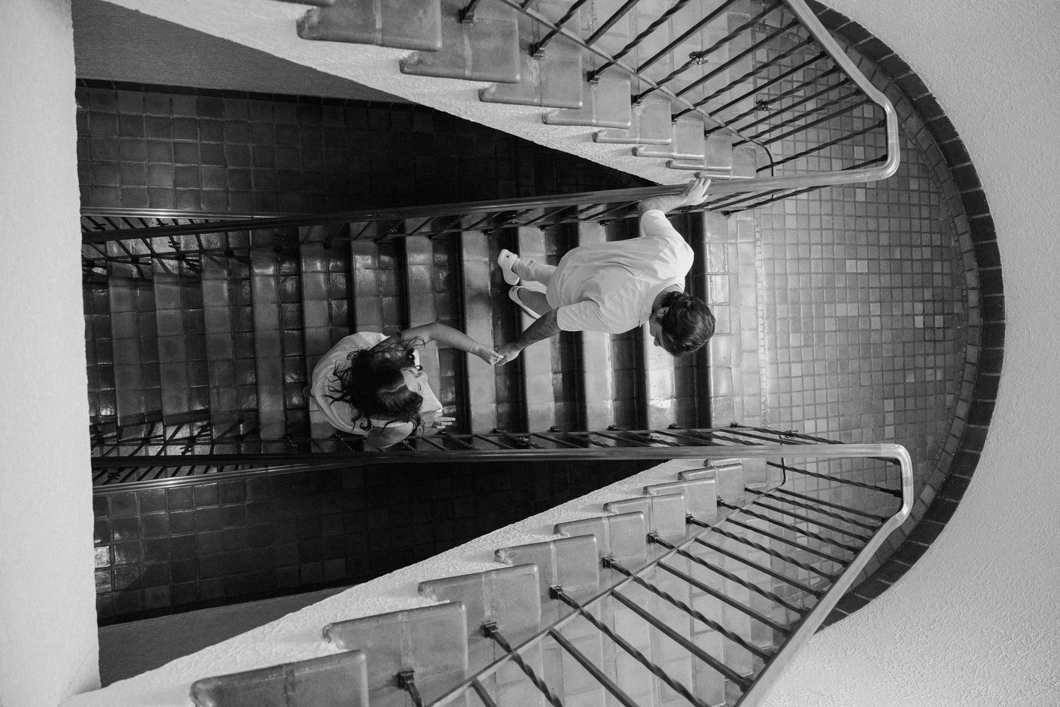 A dramatic black and white overhead view of curved staircases creating a geometric spiral pattern reflected in water below.